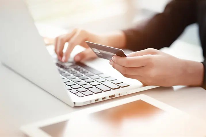 Person hält eine Zahlungskarte in der Hand und nutzt gleichzeitig ein Notebook für einen Onlinekauf