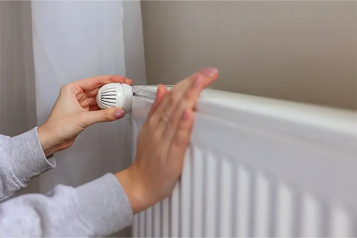Hände drehen ein Thermostat an einem Heizkörper zur Temperatureinstellung.