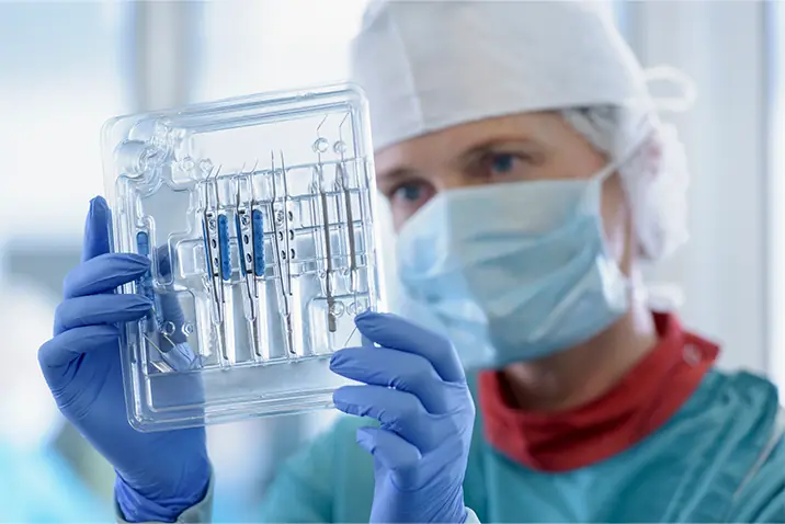 Person mit Schutzkleidung prüft sterile medizinische Instrumente in einer Verpackung